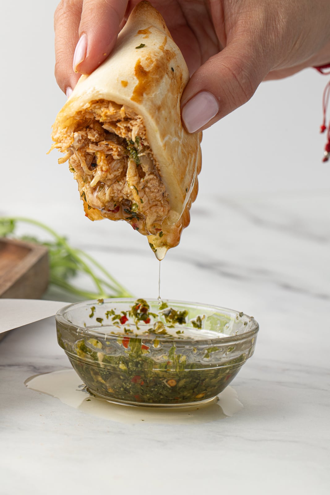 A chicken empanada dipped in chimichurri